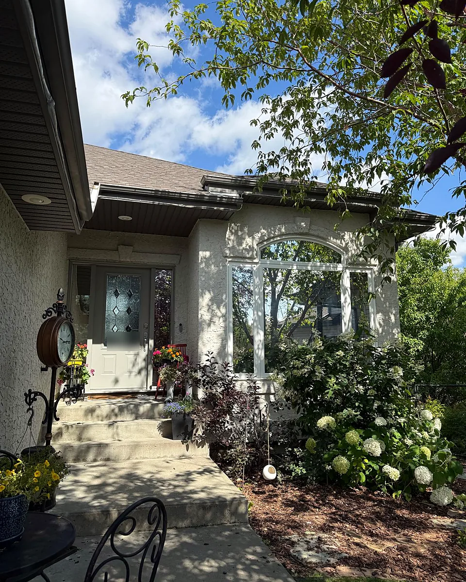 Stucco home with an arched front window and a glass front door, surrounded by garden