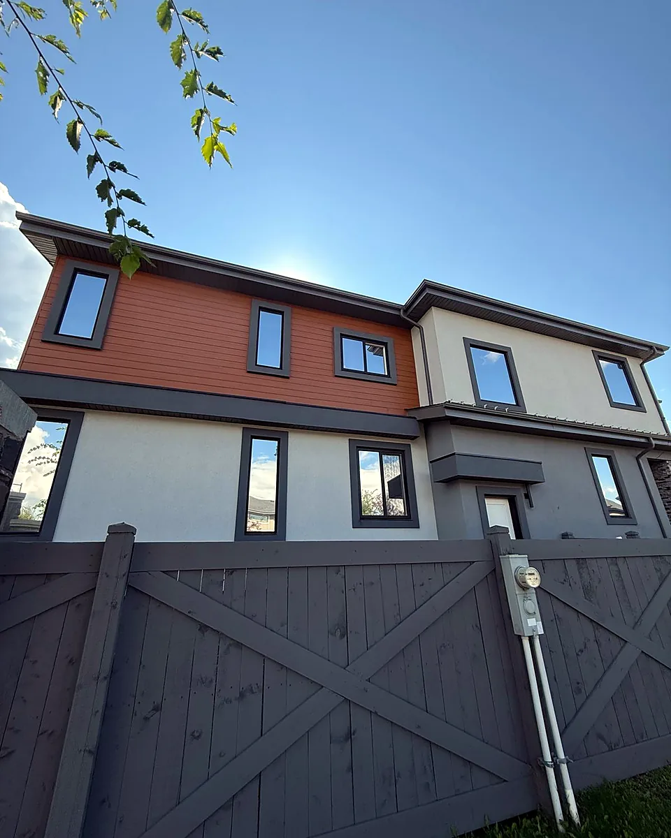 Modern two-story home with tinted windows on both floors behind a gray fence